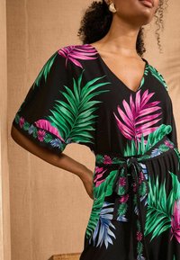 Čierne šaty so živými ružovými a zelenými tropickými listovými potlačami, krátke rukávy, výstrih do V a s opaskom v páse.
