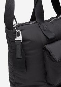 Sort nylon taske med quiltet tekstur, sølv hardware, topzip-lukning og justerbare stropper. Har en frontlomme med klap.
