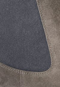 Bota de ante con un exterior suave de color gris. Presenta un inserto de tela oscura y suave, bordes cosidos y un diseño elegante.