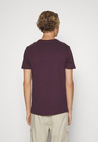 T-shirt à manches courtes et col rond de couleur prune riche, en coton doux, avec un design uni sans motifs ni accessoires notables.