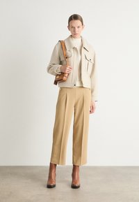 Beige cropped jakke med to lommer, cremet ribbestrikket sweater, brune vide bukser og brune ankelstøvler. Brun taske med guldfarvede detaljer.