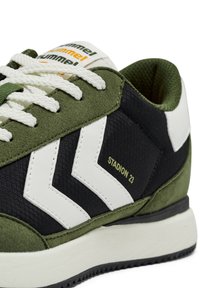 Zielono-czarne buty sportowe z białymi szczegółami w kształcie chevronu, teksturowana tkanina, zamszowe akcenty i kontrastowe sznurowadła. Posiadają napis "STADION 23".