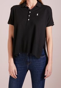 Schwarzes Poloshirt aus weichem Stoff, mit Kragen, kurzen Ärmeln, einer Drei-Knopf-Leiste und einem kleinen weißen Logo auf der linken Brust.
