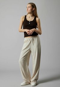 Zwarte geribbelde tanktop met drie knopen, gecombineerd met lichtgewicht crèmekleurige broek met trekkoord en witte sneakers.