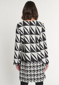 Černobíle vzorovaná šaty s geometrickými designy, dlouhými rukávy a detailem ve tvaru klíčové dírky na zádech. Měkká, texturovaná tkanina.