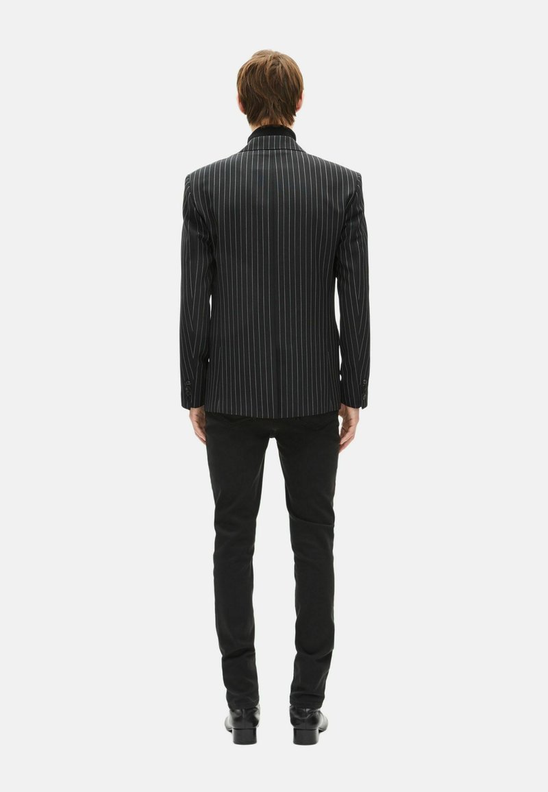 Blazer à fines rayures noires avec épaules structurées et col à revers en encoche, porté avec un pantalon noir, vu de dos. Texture de tissu lisse.