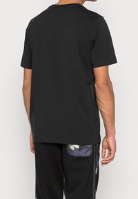 Černé bavlněné tričko s kulatým výstřihem, krátkými rukávy a jednoduchým designem na zadní straně. Tkanina vypadá měkce a má standardní střih.