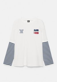 Chemise blanche à manches longues avec manches rayées bleu marine et blanc, texte « NOUS PRENONS SOIN DE VOS MARCHANDISES » et lettres style ballons rouges, blanches et bleues sur la poitrine.