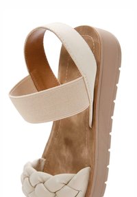Sandalo platform color crema con parte anteriore in pelle intrecciata, cinturino elastico alla caviglia e suola beige texturizzata. Rivestimento interno morbido.