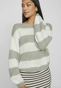 Leichter Strickpullover mit horizontalen grauen und weißen Streifen, weitem Ausschnitt und lockeren Ärmeln. Kombiniert mit einem gestreiften, taillierten Rock.