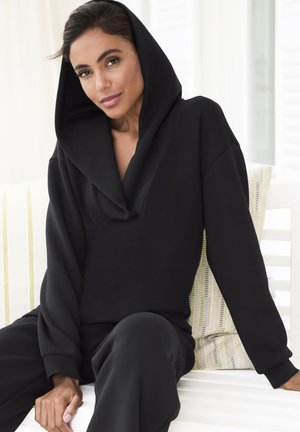 Schwarzer Kapuzensweatshirt mit tiefem Cowl-Hals und lockeren Ärmeln, kombiniert mit passenden schwarzen Hosen. Glatte Textur, entspannte Passform.