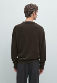 Maglione a maglia marrone con vestibilità comoda, polsini e orlo a costine, e scollatura rotonda, abbinato a pantaloni scuri, visto da dietro.