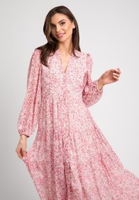 Lekka różowa sukienka w kwiatowy wzór, z dekoltem w serek i długimi bufkami na rękawach. Posiada wykończoną warstwami spódnicę oraz guziki z przodu.