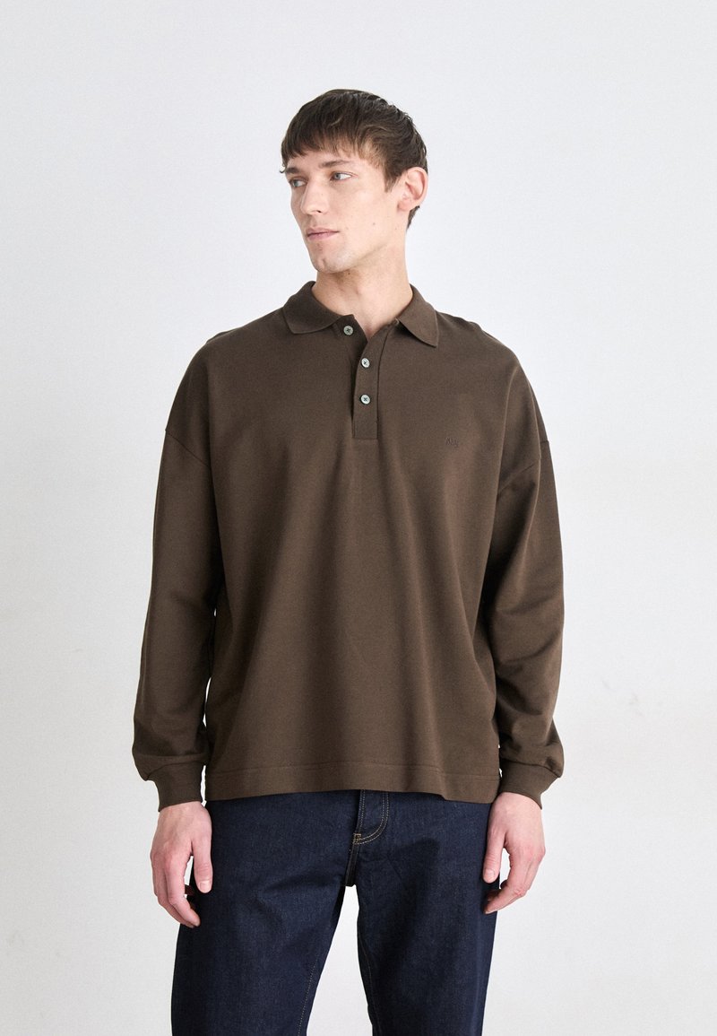 Brun langermet polo skjorte med krage, tre knapper og subtil logo. Brukt med mørke denim jeans. Glatt stoff tekstur.