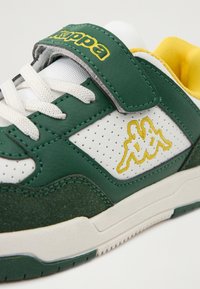 Πράσινα και λευκά αθλητικά παπούτσια με βέλκρο λουρί, από υλικά υφασματοποιημένου δέρματος και σουέτ, διαθέτουν κίτρινη κεντητή λογότυπο και διάτρητες λεπτομέρειες.