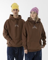 Felpe marroni con tasche frontali e loghi ricamati, abbinate a pantaloni di denim con un motivo. Berretti di maglia gialli e rosa.