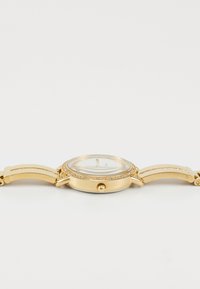 Gold metal watch with a round face, clear crystal display, and bezel adorned with small crystals. Smooth linked strap design.