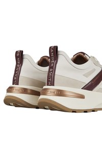 Sneaker bianchi con una texture liscia, caratterizzati da dettagli bordeaux e una suola in bronzo metallizzato, logo del marchio in rilievo sul tallone e sui pannelli laterali.