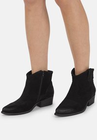 Botines de ante negro con puntera ligeramente puntiaguda, cierre de cremallera, detalles de costuras curvadas y tacón apilado.