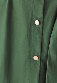 Tessuto verde con una texture liscia presenta bottoni dorati lungo il lato, evidenziando un design semplice e funzionale.