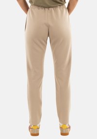 Pantalones de chándal beige con cintura elástica y bolsillos laterales, diseño de pierna ajustada. Llevados con zapatillas coloridas que tienen una suela de goma.