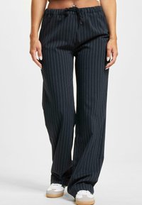 Sorte stripete videbukser med elastisk midje og snor. Kombinert med hvite joggesko og har en glatt tekstur.