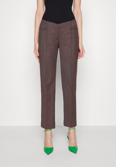 Καφέ και κόκκινες υφασμάτινες παντελόνες προσαρμοσμένες με σχεδίαση ίσιας γραμμής, με δύο μπροστινές τσέπες και συνδυασμένες με πράσινα μυτερές γόβες.