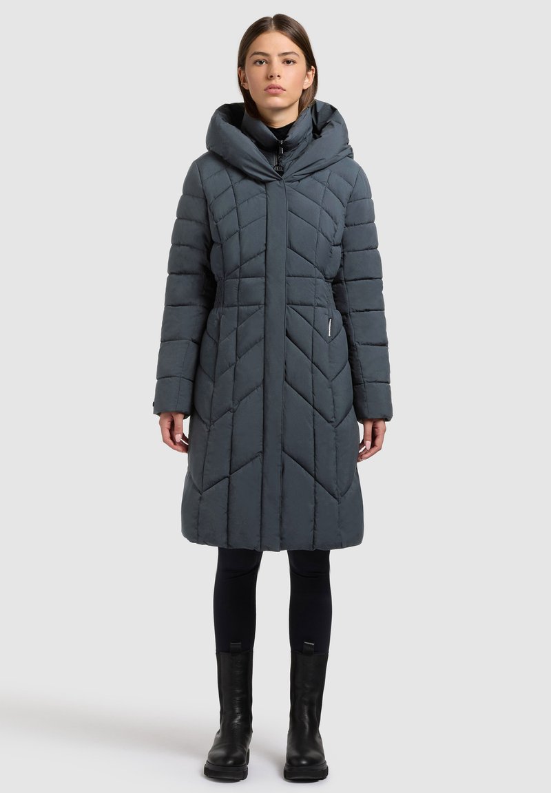 Napihnjena kapuca z ogrinjalom v temno sivi barvi z vzorcem cik-cak, sprednjo zadrgo in dvema stranskima žepoma. Poudarek je na sproščenem kroju in srednji dolžini.