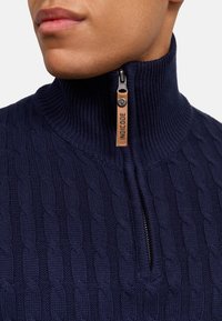 Pull marine à col montant et demi-zip, avec un motif en tricot torsadé texturé et une tirette en cuir.