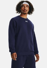 Sudadera de felpa de color azul marino con puños y dobladillo acanalados, con un logo blanco en el pecho. El diseño incluye un cuello redondo y mangas largas.