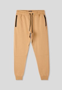 Pantaloni sportivi beige fino al ginocchio con vita elastica e tasche con zip nere su ciascun lato. Cuffs aderenti alla caviglia. Texture morbida.