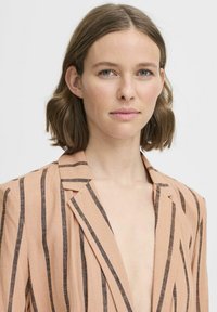 Blazer a righe pesche con linee nere, in tessuto leggero, colletto a punta e design aperto, caratterizzato da una vestibilità comoda e una consistenza morbida.