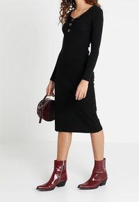 Černé ribované midi šaty s dlouhými rukávy a detailem tří knoflíků. Kombinováno s lesklými bordó kotníkovými botami a kulatou kabelkou.