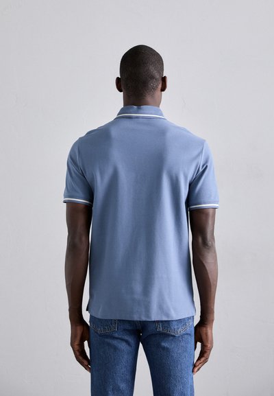 Polo de culoare albastră, cu o textură moale, având guler și margini contrastante la mâneci. Asortat cu blugi din denim albastru.