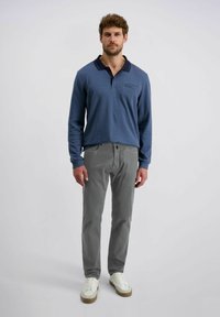 Polo a maniche lunghe azzurro chiaro con colletto scuro, abbinato a pantaloni grigi chiari e sneaker bianche. Tessuto morbido con un design a vestibilità rilassata.