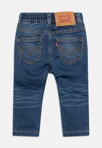 Vaqueros de mezclilla de color azul oscuro, corte ajustado, con cinturilla elástica y dos bolsillos traseros adornados con costuras y una etiqueta de cuero de marca.