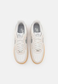 Nike Air Force 1-sneakers har ett ovandel i vitt läder med grå detaljer, en perforerad tå och en sula av gummi.