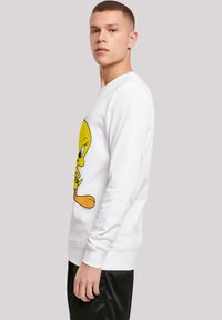 Hvit hettegenser med lange ermer som har en stor, fargerik Tweety Bird-grafikk på fronten. Glatt bomullstoff, ribbestrikkede mansjetter og hem.