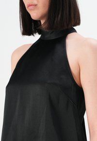 Sort ærmeløs top med høj halsudskæring, som har et glat, tekstureret stof og minimalistisk design. Fremhæver skuldrene og kravebenet.