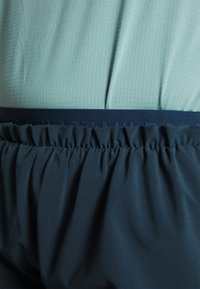 Kortärmad skjorta i ljusgrön meshväv med midja i mörkblått, kombinerad med marinblå shorts med en samlad elastisk midja.