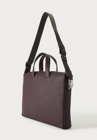 Serviette en cuir brun foncé avec double poignée supérieure et bandoulière en tissu sombre réglable, sur un fond clair.