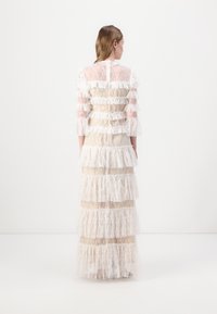 Rochie lungă cu un design din dantelă transparentă, având volane orizontale și mâneci lungi. Culoare albă cu texturi stratificate și închidere la spate.