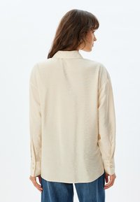 Crème-kleurige blouse met lange mouwen, een zachte textuur, een kraag en knoopmanchetten. Losse pasvorm met een licht gebogen zoom.