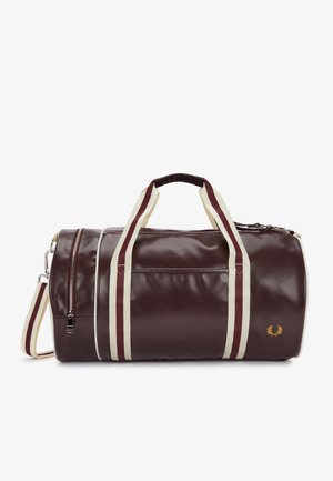 Bolsa de viaje cilíndrica de color marrón oscuro, con asas a rayas crema y burdeos, una correa para el hombro, bolsillos con cremallera y un pequeño emblema dorado.
