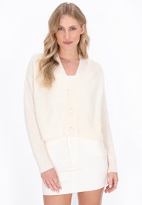 Cardigan accorciato color crema con una texture a costine, ampio colletto a scialle e tre bottoni extra-large sul davanti. Tessuto liscio.