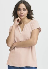 Top corto a maniche corte di colore rosa chiaro con scollo a V, taschino sulla parte sinistra del petto e texture morbida, abbinato a jeans blu di denim.
