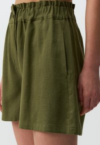 Pantaloni corti in lino verde con vita elastica e tasche laterali. Il tessuto presenta una sottile trama ed una vestibilità comoda con orli leggermente arrotolati.