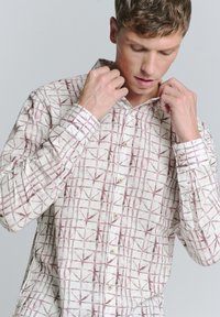 Hemd met lange mouwen van lichte stof, met een witte basis en een rood geometrisch rasterpatroon, knoopsluiting en puntige kraag.