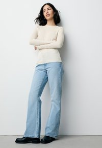 Bluză crem cu mâneci lungi și dungi, asortată cu blugi evazați bleu deschis și ghete negre până la gleznă. Croiala este lejeră, sporind confortul și libertatea de mișcare.