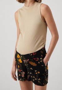 Beige pruhovaný top bez rukávů, který je spárován s černými květinovými šortkami s žlutými a růžovými květy, bočními kapsami a elastickým pasem.